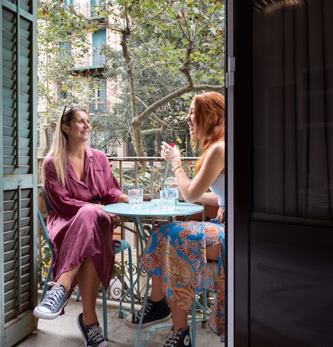 A bright picture of two girls sitting on a blue table on the balcony